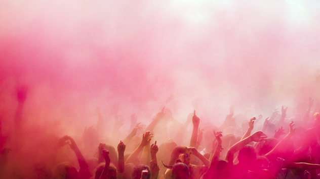 Crowd of people with raised arms surrounded by thick pink and red coloured powder paint creating a vibrant haze that fills the air.