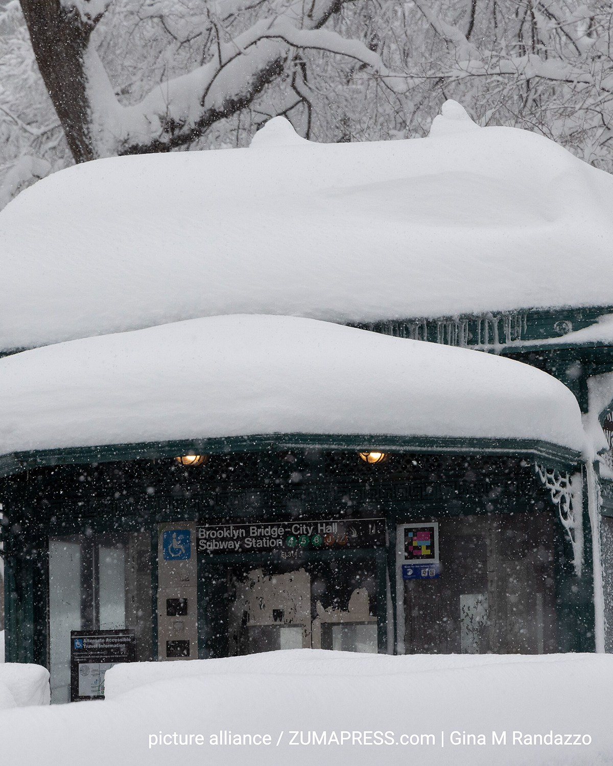 Ingang van het metrostation Brooklyn Bridge–City Hall in Manhattan, volledig bedekt met sneeuw. Dikke lagen sneeuw liggen op het dak en de leuningen, hevige sneeuwval vermindert het zicht. Bomen op de achtergrond zijn ook zwaar bevroren en besneeuwd.