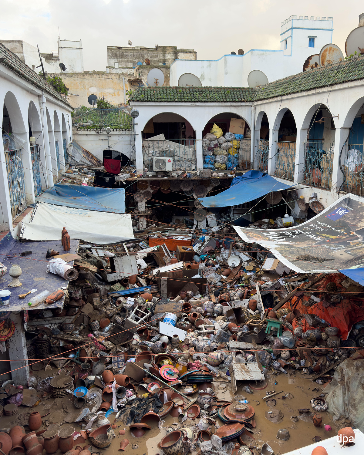 Flooded market courtyard littered with broken ceramics and debris. Damaged arcades and tarpaulins hang over the destroyed area.