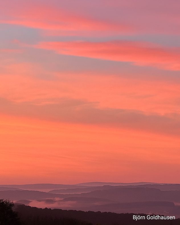 Roter Morgenhimmel über nebligen Hügeln in sanftem Licht.