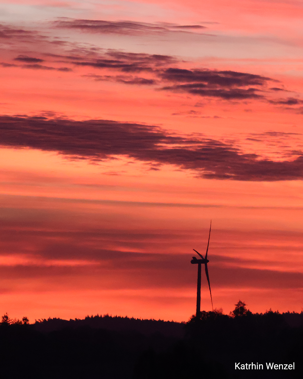 © Kathrin Wenzel Windrad vor rotem Morgenhimmel mit leuchtenden Wolkenschichten.