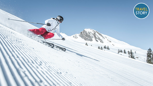 Eine Skifahrerin auf einer frisch präparierten Piste - im Hintergrund schneebedeckte Berge. 
