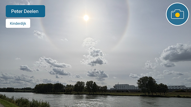 Een foto van een fraaie kring om de zon boven het water in een melkachtig witte lucht.