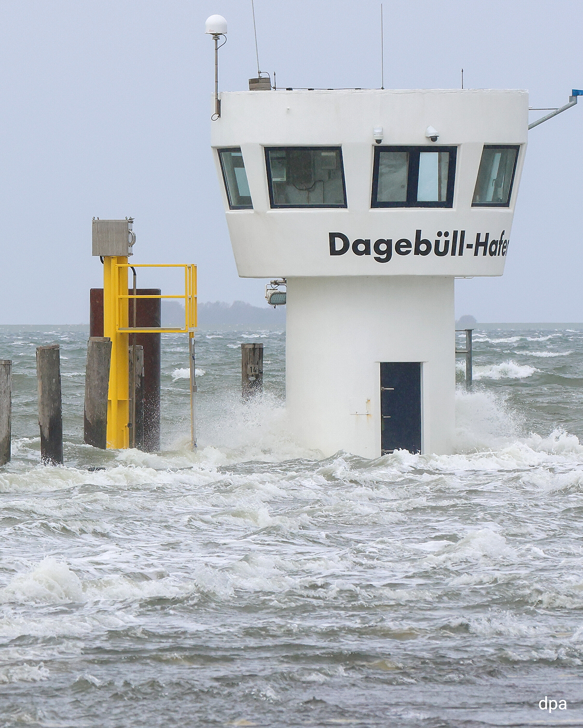 Hoher Wellengang im Hafen von Dagebüll, Wasser umspült den Kontrollturm, grauer Himmel und stürmische See.