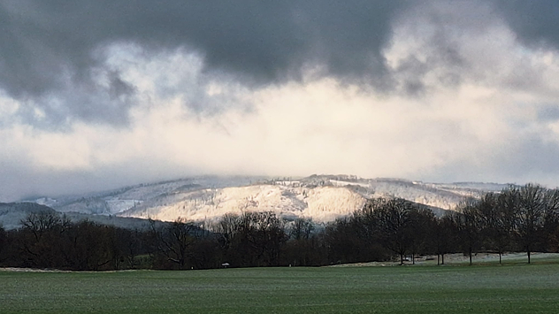 © Wiebke Müller Verschneite Hügel unter dunklen Wolken, von Sonnenlicht durchbrochen.
