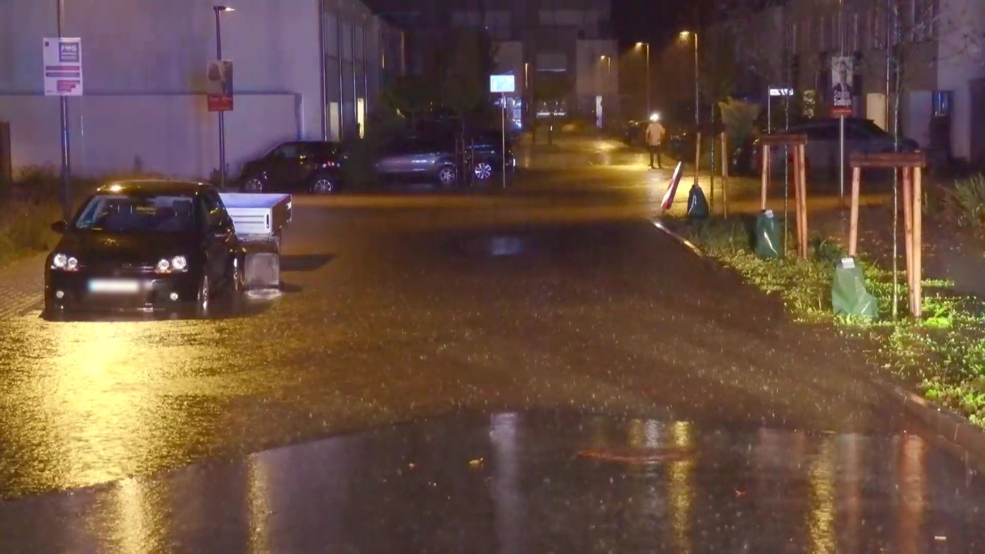 Überflutete Straße bei Nacht mit parkenden Autos und Laternenlicht.
