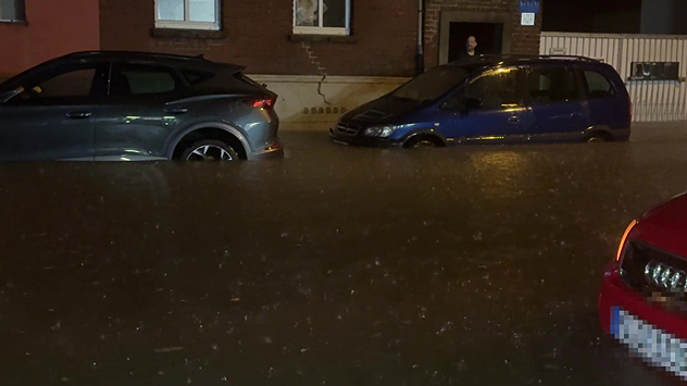 Autos stehen in einer überfluteten Straße vor Häusern.