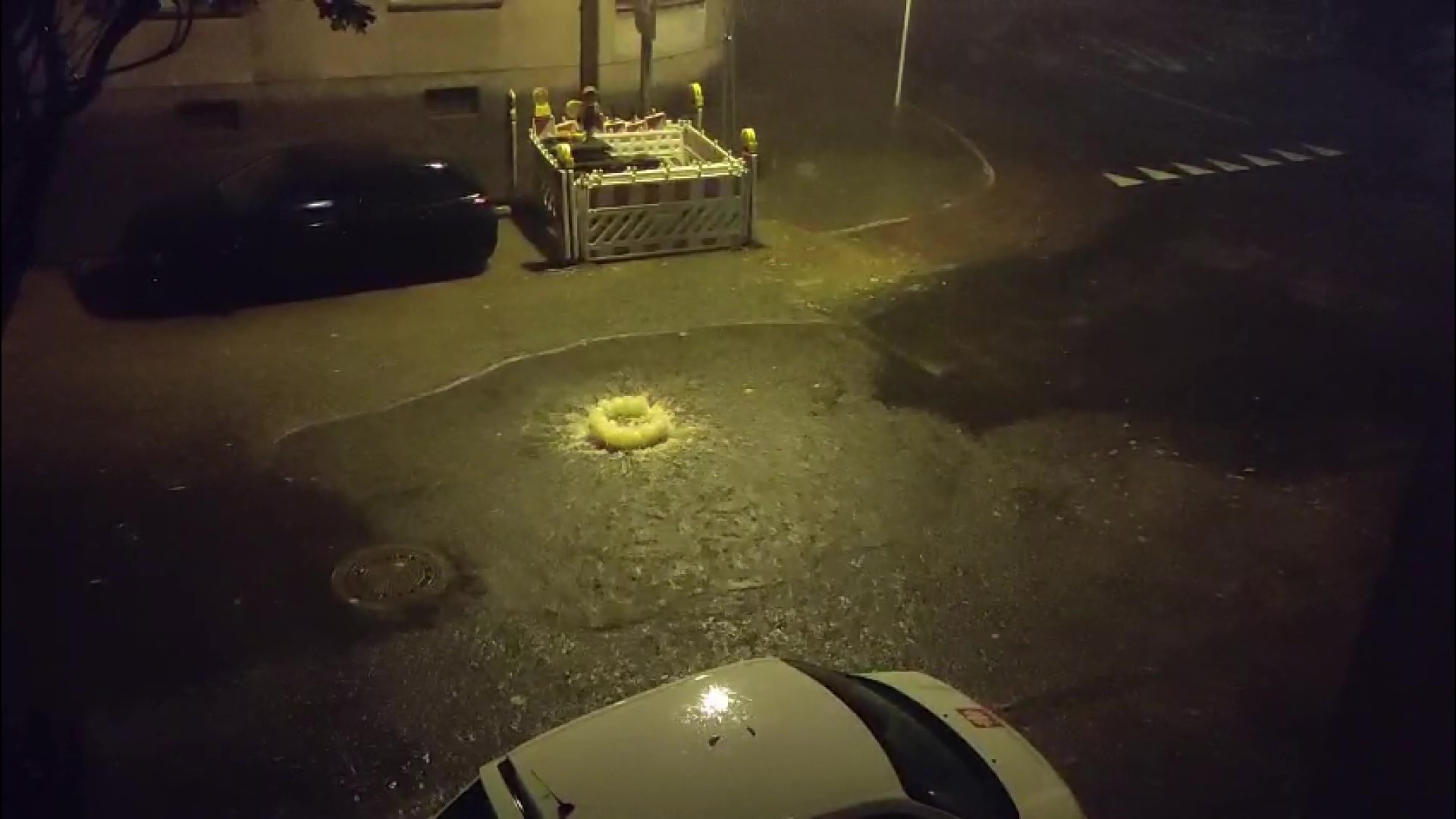 Wasser strömt bei Nacht aus einem Kanaldeckel auf die Straße.