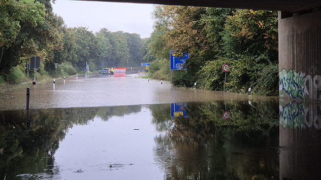 Überflutete Unterführung mit Straßensperre und Polizeifahrzeug im Hintergrund.