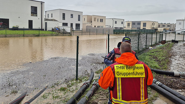 THW-Helfer mit Pumpenschläuchen vor überfluteten Wohnhäusern.