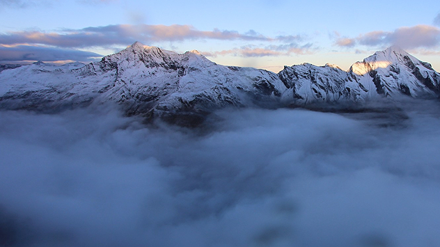 Schneebedeckte Berge im Morgenlicht und Wolken im Tal