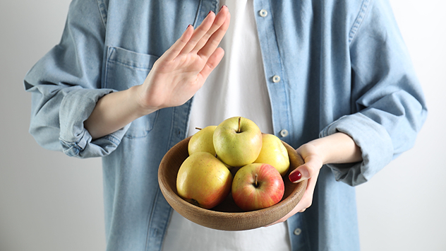 Person mit Schale voller Äpfel hebt abwehrend die Hand. Darstellung einer Kreuzreaktion bei Pollenallergie. Symbol für allergische Reaktion auf Obst.