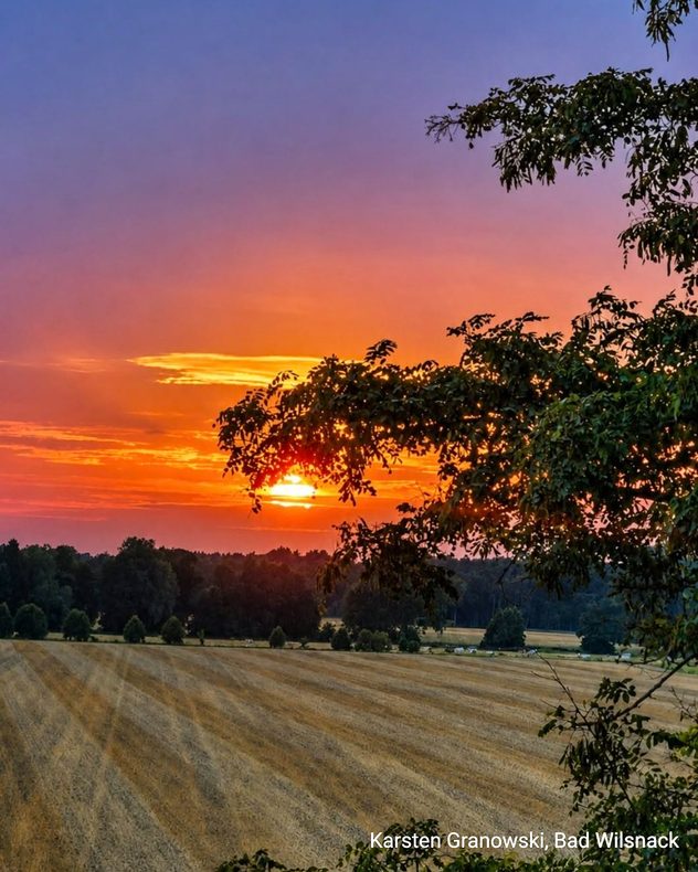 Die Sonne geht an glühendem Himmel unter. Der Farbverlauf geht von oben blau nach unten orange.