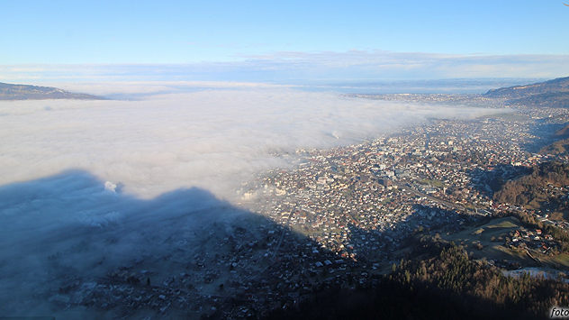 Blick von einem Berg auf eine Stadt, die zur Hälfte von einer niedrigen Wolkenschicht bedeckt ist.