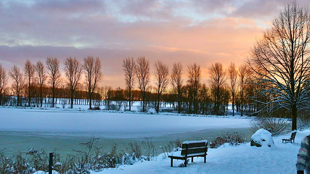 Winterlandschaft am Elkenrother Weiher am 4. Januar 2026: Der See ist teilweise zugefroren und mit Schnee bedeckt, doch das Betreten der Eisfläche ist gefährlich – das Eis wirkt dünn und nicht tragfähig. Die untergehende Sonne färbt den Himmel rosa-orange.