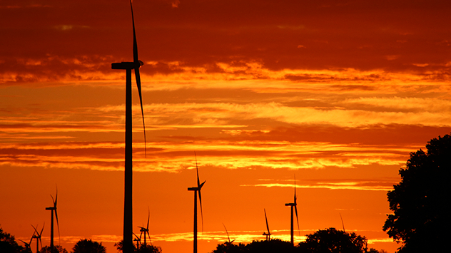 Silhouetten von Windrädern vor einem intensiv orangen Sonnenuntergang.