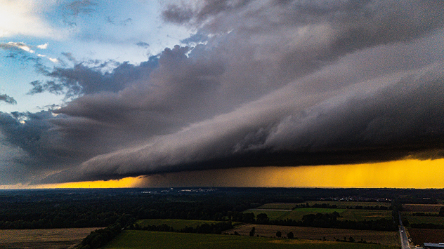 Eine massive Gewitterwolke zieht über die Landschaft, der Horizont leuchtet gelb-orange.