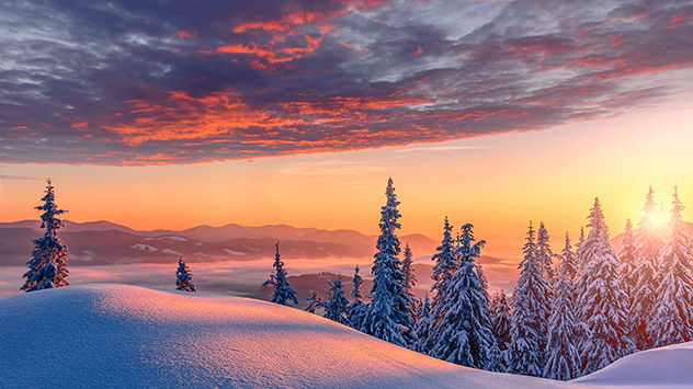 Sonnenuntergang vor verschneiter Winterlandschaft.