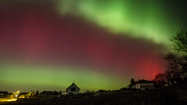 Grün-rote Polarlichter über Häusern in einer Siedlung bei Nacht.