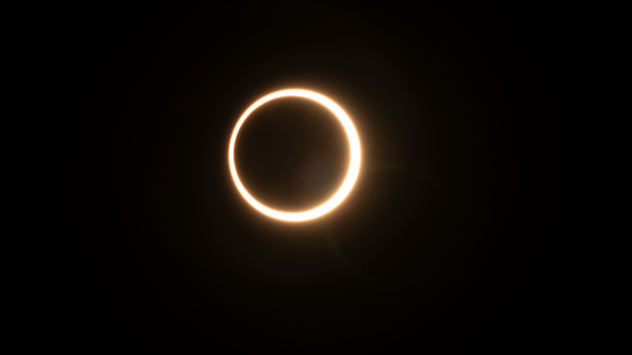Annular solar eclipse against a black sky, with the Moon centered over the Sun and a bright golden ring of sunlight visible around its edge.