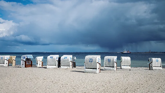 Strandkörbe an der Küste. Am Himmel sind dunkle Wolken und ein Schauer zu sehen.