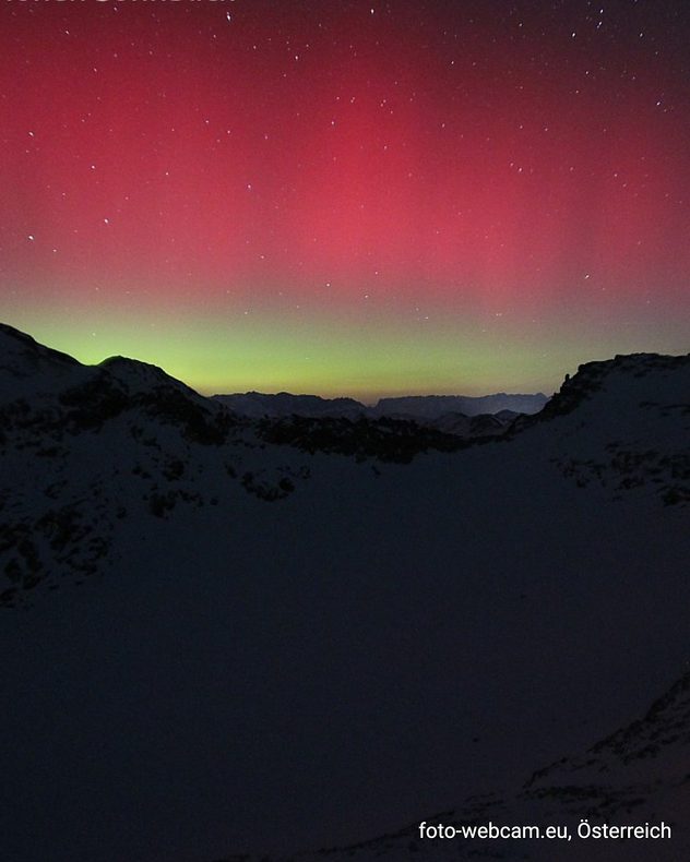 Aurores boréales rouges et vertes au-dessus des Alpes enneigées la nuit.