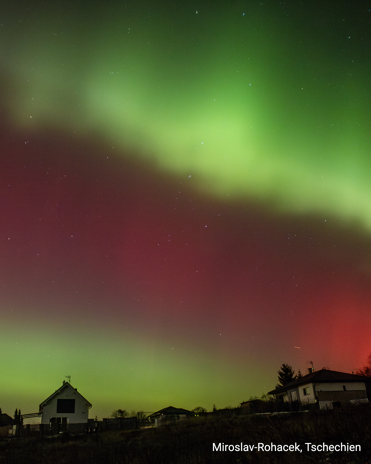Aurore boréale verte et rouge au-dessus des maisons la nuit. Zone résidentielle en République tchèque.