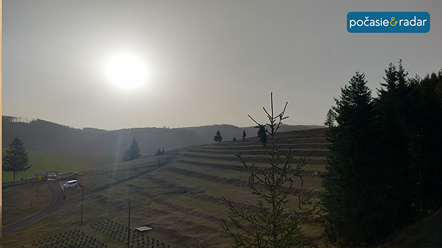 Slnko presvitajúce cez saharský prach nad kopcovitou krajinou so zníženou dohľadnosťou