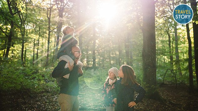 Ein Vater mit drei Kindern im Wald, die Sonne scheint durch die Baumwipfel. (c) TMV/Gross