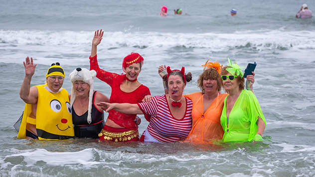 Kostümierte Eisbader vergnügen sich beim traditionellen Faschingsbaden in der Ostsee am Strand von Warnemünde.