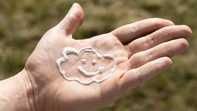 Eine Handfläche mit Sonnencreme, die in Form einer Wolke mit lächelndem Gesicht aufgetragen wurde. 