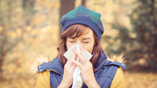 Eine Frau, die sich bei herbstlichem Wetter die Nase putzt. 