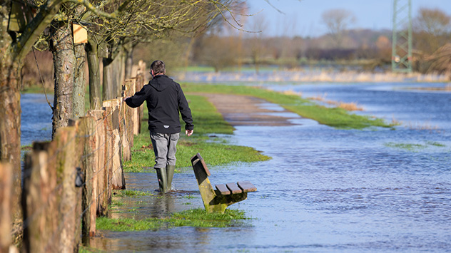 Ein Mann watet mit Gummistiefeln durch das Wasser. Noch sind viele Felder und Wiesen überschwemmt und nicht alle Straßen wieder trocken. 