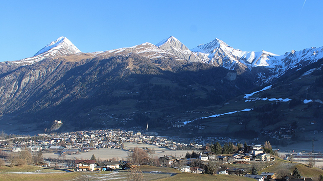 Blick auf Matrei in Osttirol vor einer teils schneebedeckten Alpenkette unter klarem Himmel.