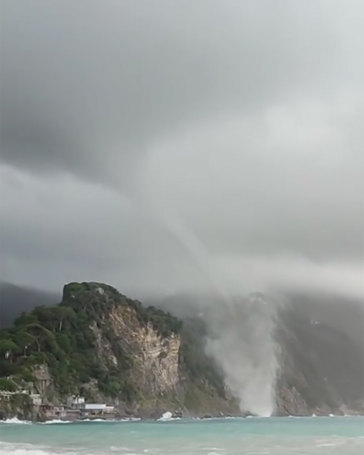 Tromba marina sul mare vicino alla costa sotto nuvole scure.