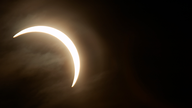 Der Mond verdeckt einen großen Teil der Sonne. Nur eine helle, schmale Sichel ist am dunklen Himmel sichtbar.