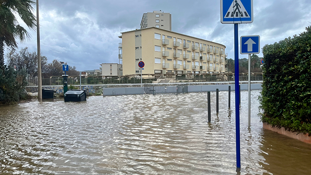 Overstroomde straat met verkeersborden en woonhuizen na aanhoudende hevige regenval.
