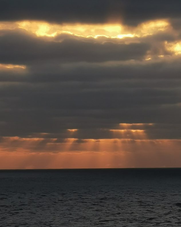 Dark clouds over the North Sea at sunset with golden sunlight streaming through the gaps in the clouds onto the water below.