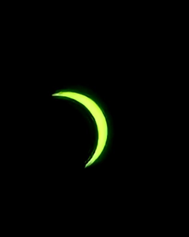 Bright green crescent of the partially eclipsed Sun against a black sky, with most of the solar disc obscured by the Moon. Pictured through a filter.