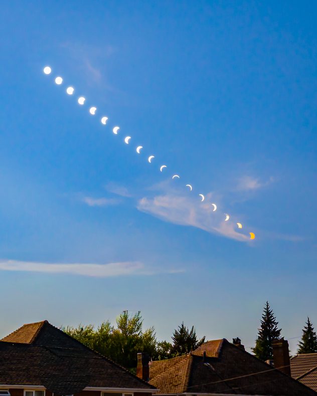 Composite sequence showing the Sun progressively obscured during a partial solar eclipse, with bright crescent phases tracing a diagonal path across a blue sky above rooftops.