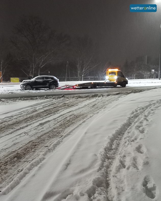 Odtahovka nakládá auto na zasněžené silnici v noci.