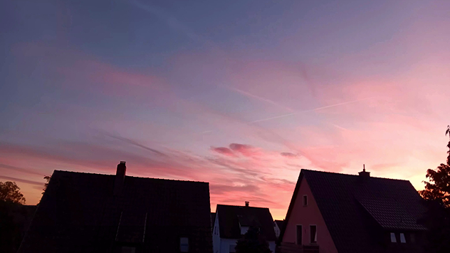 © Renate Andres via WetterMelder Deutschland Rötlich-violetter Himmel bei Sonnenuntergang. Im Vordergrund dunkle Dächer von Einfamilienhäusern.