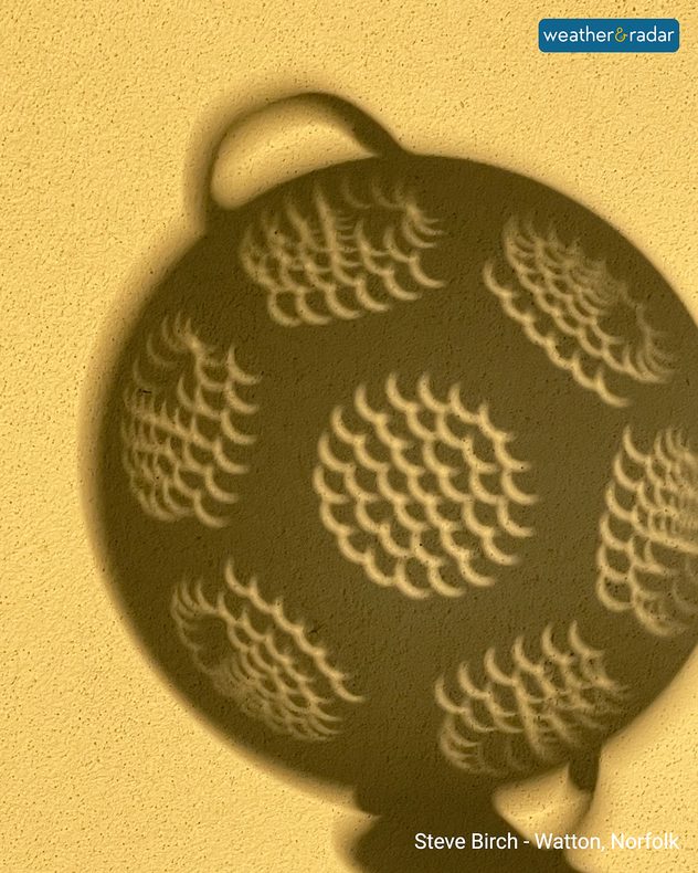 Repeated crescent-shaped partial solar eclipse projections cast across the shadow of a round garden object on a sunlit wall.