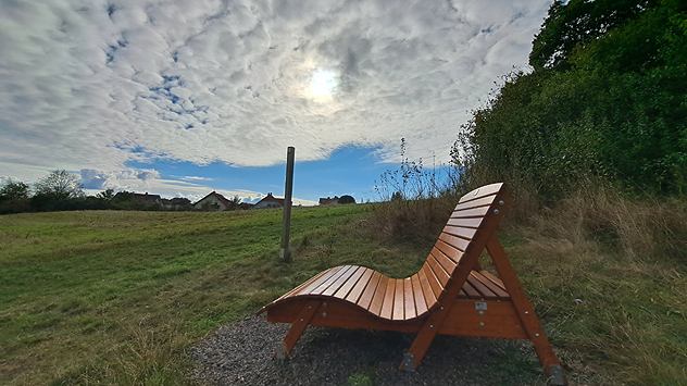 © Kathrin Wenzel Sitzbank auf einem Feld nahe Wohngebiet, Schäfchenwolken überziehen den Himmel