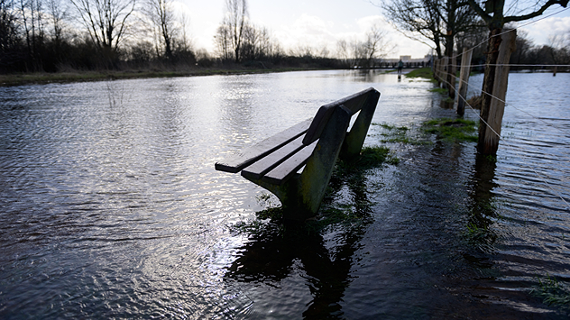 Parkbank steht am Fluss unter Wasser