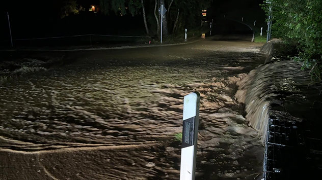Überflutete Straße bei Nacht mit starkem Wasserfluss.