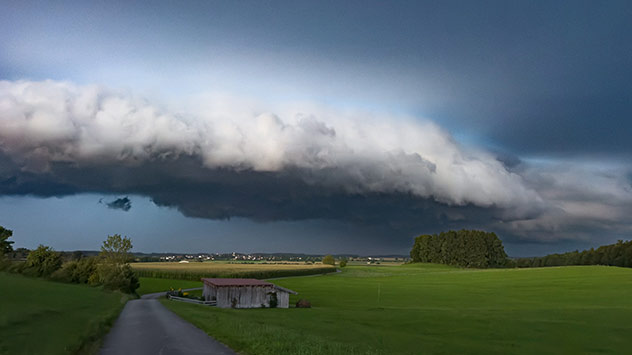 Dunkle Gewitterfront über grüner Landschaft mit kleinem Gebäude.
