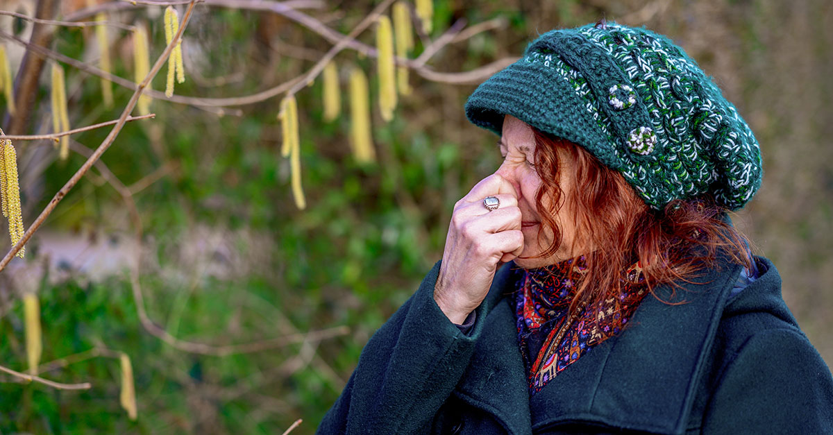 Frau hält sich Nase vor Haselstrauch zu