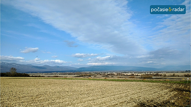 Rozľahlé pole pod čiastočne oblačnou oblohou, v pozadí pohorie