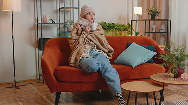 Frau in Decke eingemummelt auf der Couch.